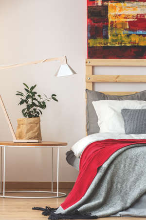 Creative trendy bedroom with plant and lamp on small table and painting above the bedの写真素材
