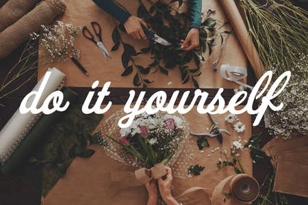 Woman showing diy flower arrangement ideas on a wooden tableの写真素材