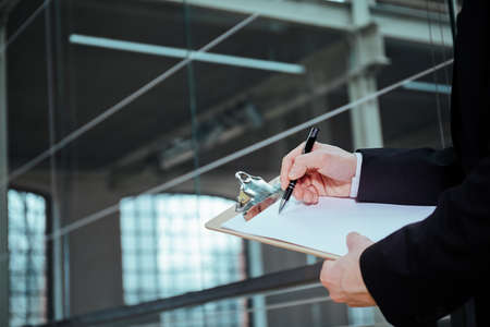 Businessman wearing suit, holding pen and clipboard, close upの写真素材