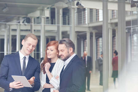 Business partners using tablet device, talking in modern office building