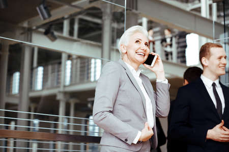Happy, mature businesswoman talking on cellphone in modern buildingの写真素材