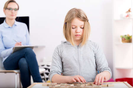Psychologist observing a little girl with building blocks with lettersの写真素材