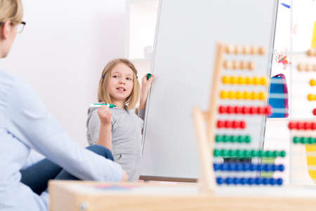 Little girl writing on whiteboard and a teacher looking at her