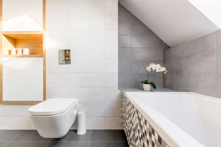 Attic bathroom in grey and white with bathtub and toiletの写真素材