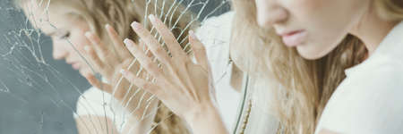 Young blonde girl touching the broken mirrorの写真素材