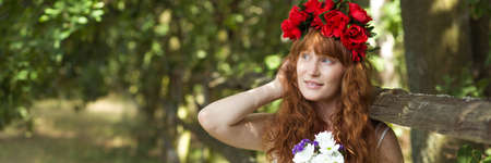 Red-haired girl with red coronet standing under the treeの写真素材