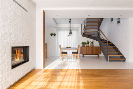 Modern, white apartment with fireplace, table and staircaseの写真素材