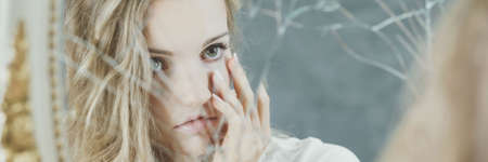 Young blonde girl looking at broken mirrorの写真素材