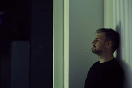 Man with a cigarette in his mouth leaning against a wallの写真素材