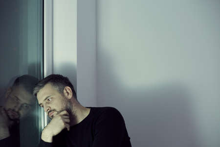 Sad lonely middle-aged man looking through the window in a room