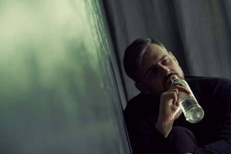 Unhappy man drinking alcohol from a bottle at nightの写真素材