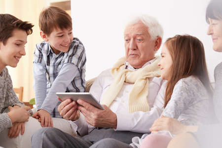 Happy children looking at their surprised grandpa holding a tabletの写真素材