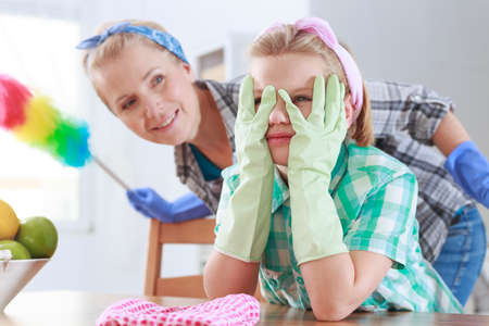 Tired girl wearing rubber gloves and her mom standing behind herの写真素材