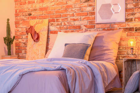 Cozy big bed by the red brick wall in stylish bedroomの写真素材