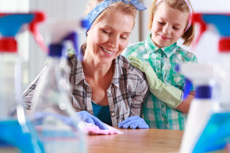Little girl wearing rubber gloves and watching her mother cleaning the table