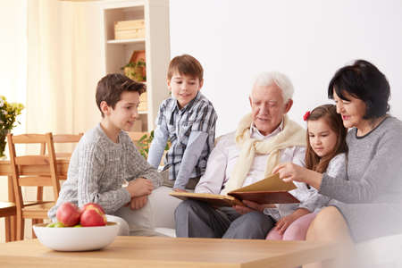 Grandparents showing family photo album to interested grandchildren