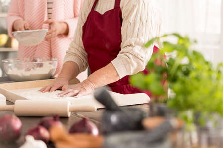 Old woman standing in a kitchen and baking a cakeの写真素材