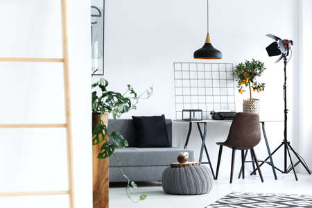 White, minimalist living room with grey sofa, lamp, desk, ladderの写真素材