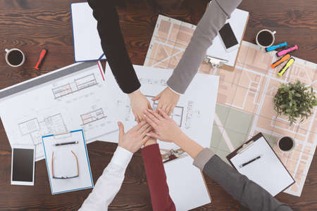 Architects making pile of hands over a wooden table with plansの写真素材