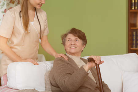 Young caregiver and senior woman with a cane in a living room