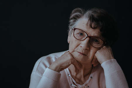 Sad, old woman wearing eyeglasses, black backgroundの写真素材