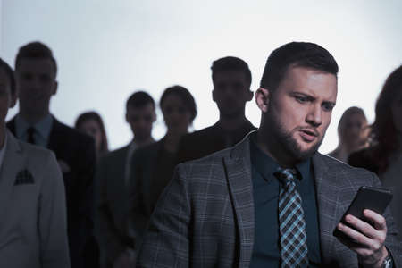 Nervous young businessman checking his phone and standing in crowd of peopleの写真素材