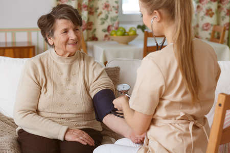 Young nurse checking senior woman's blood pressure in a living room