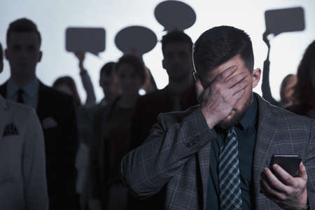 Young man covering his face and standing against blurred crowdの写真素材