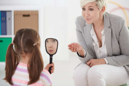 Woman talking with girl holding mirror in her handの写真素材