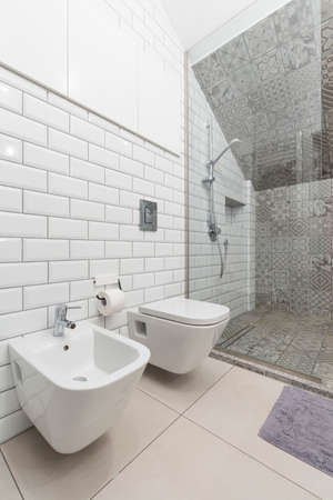 White brick tiles in creative bathroom with toilet and glass shower cabin