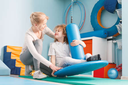 Boy sitting on swing, exercising with physiotherapistの写真素材