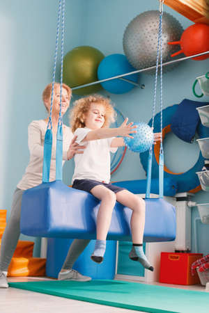 Boy exercising with ball, sitting on therapeutic swingの写真素材