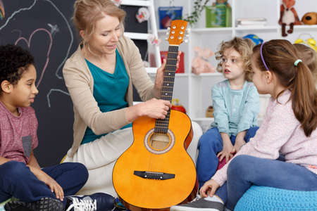 Kindergarten teacher showing kids how to play the guitarの写真素材