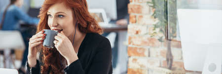 Beautiful young woman drinking coffee in modern office