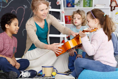 Little preschool girl holding teacher's guitar on music lessonの写真素材