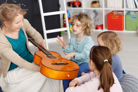 Young teacher having music lesson with small kids in kindergartenの写真素材