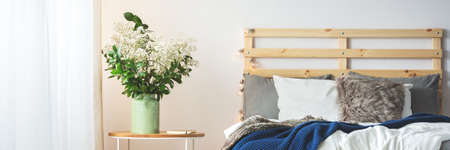 White flowers on a nightstand by the cozy wooden bed
