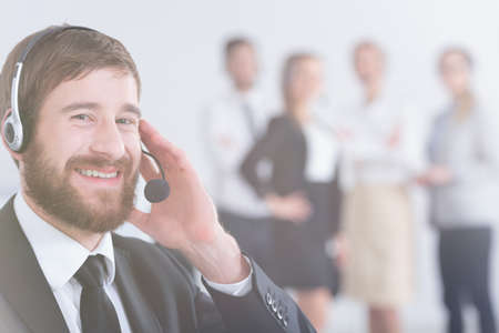 Smiling man working in call center with team in backgroundの写真素材