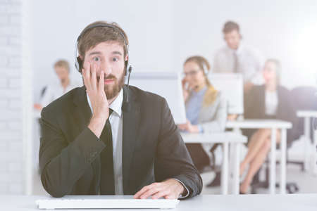 Worried confused hotline agent at work in modern business call centerの写真素材