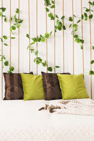 Bedroom with bed, green and brown pillows, rope wall, ivy