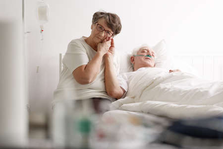 Elderly loving wife tenderly holding hand of sick senior manの写真素材