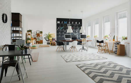 Black and white creative workspace with desks, chairs, computers, rugsの写真素材