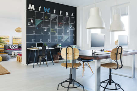 Open workspace with blackboard wall, desk, chairs, computersの写真素材