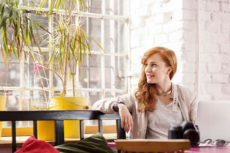 Pretty young woman with photo camera sitting in loft apartmentの写真素材