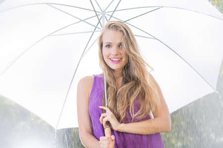 Blonde woman with white umbrella standing in the rainの写真素材