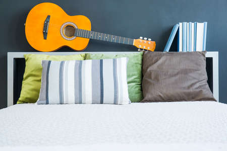 White bed with pillows and headboard with guitar and books on itの写真素材