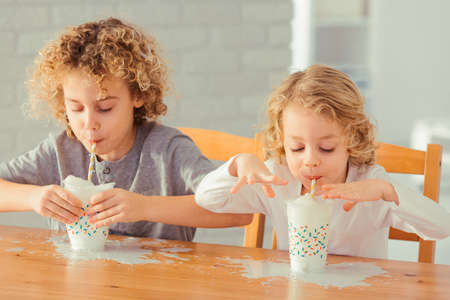 Two little boys spilling milk on the kitchen tableの写真素材