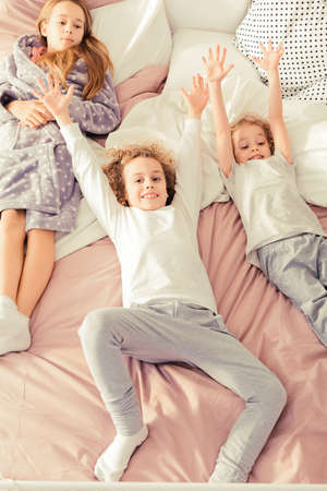 Cute siblings smiling and resting on the bedの写真素材