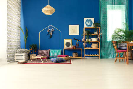 Postcolonial style apartment with blue wall, wooden furniture, pattern cushionsの写真素材