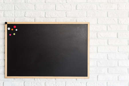 Blackboard with colorful magnets hanging on white brick wallの写真素材